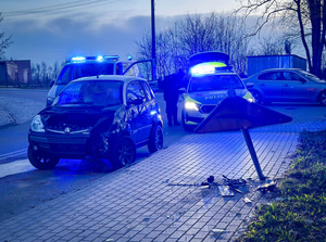 Uszkodzone auto i znak drogowy. Za nimi dwa radiowozy.
