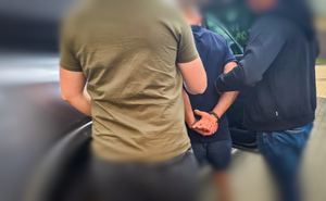 Mężczyzna trzymany przez policjantów wsiada do samochodu.